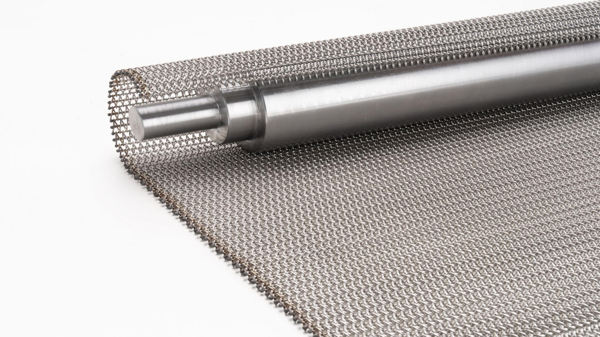 A roll of fine metallic wire mesh is partially unrolled on a white surface, showing its woven texture and a cylindrical metal core.