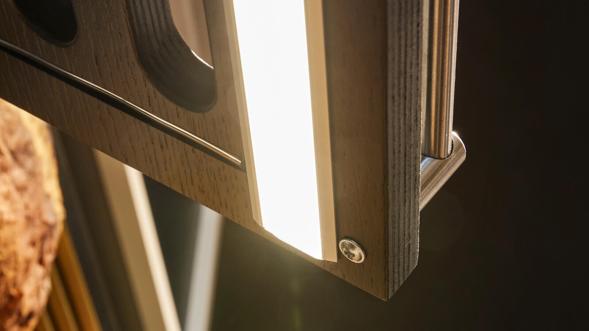 Nahaufnahme einer Holzplatte mit einem eingebauten hellen LED-Lichtstreifen, einer Metallhalterung und einer sichtbaren Schraube an der Ecke, wobei weiches Sonnenlicht die Szene von der Seite beleuchtet.