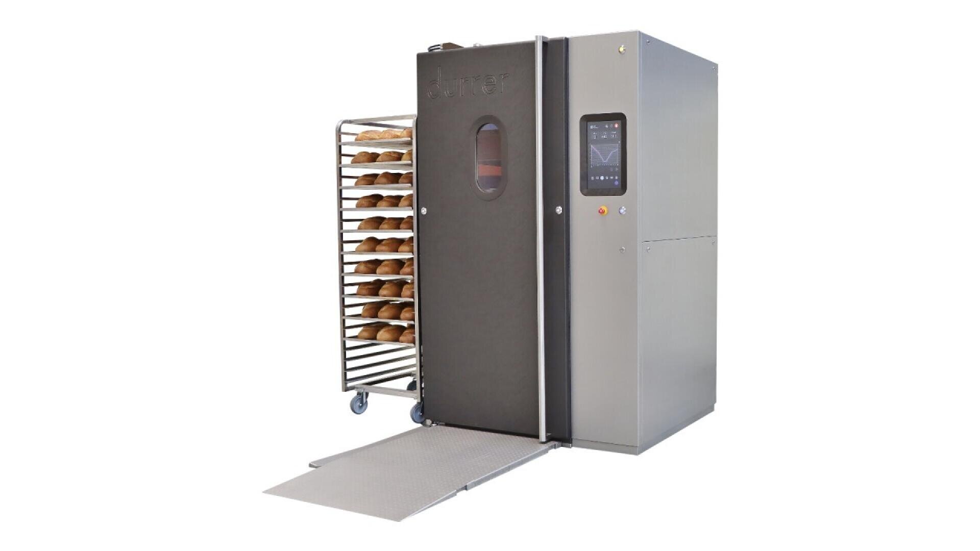 A commercial bread oven with a digital control panel, open door, and a metal ramp leading to a wheeled rack filled with freshly baked loaves of bread. The oven and rack are set against a white background.