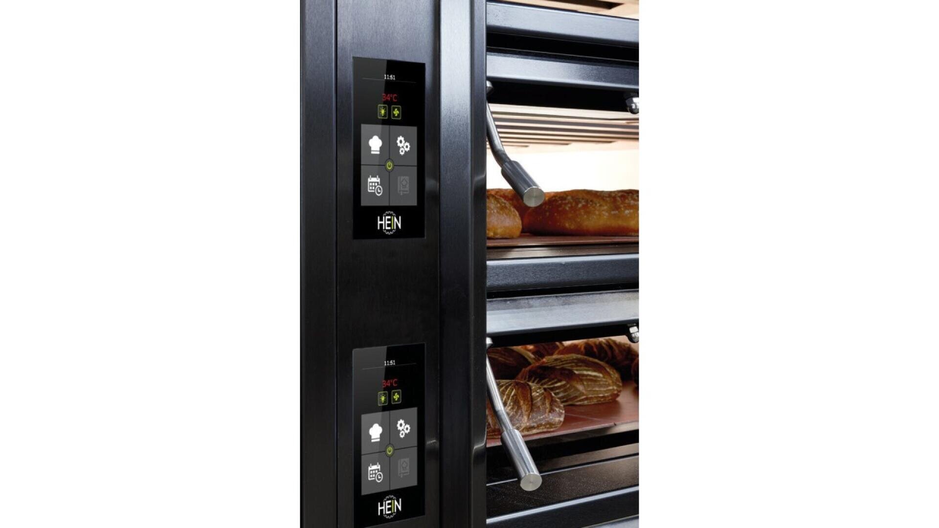 Close-up of a modern commercial oven with digital control panels and two shelves, each holding freshly baked loaves of bread. The oven has a sleek, black exterior and clear glass doors displaying the bread inside.