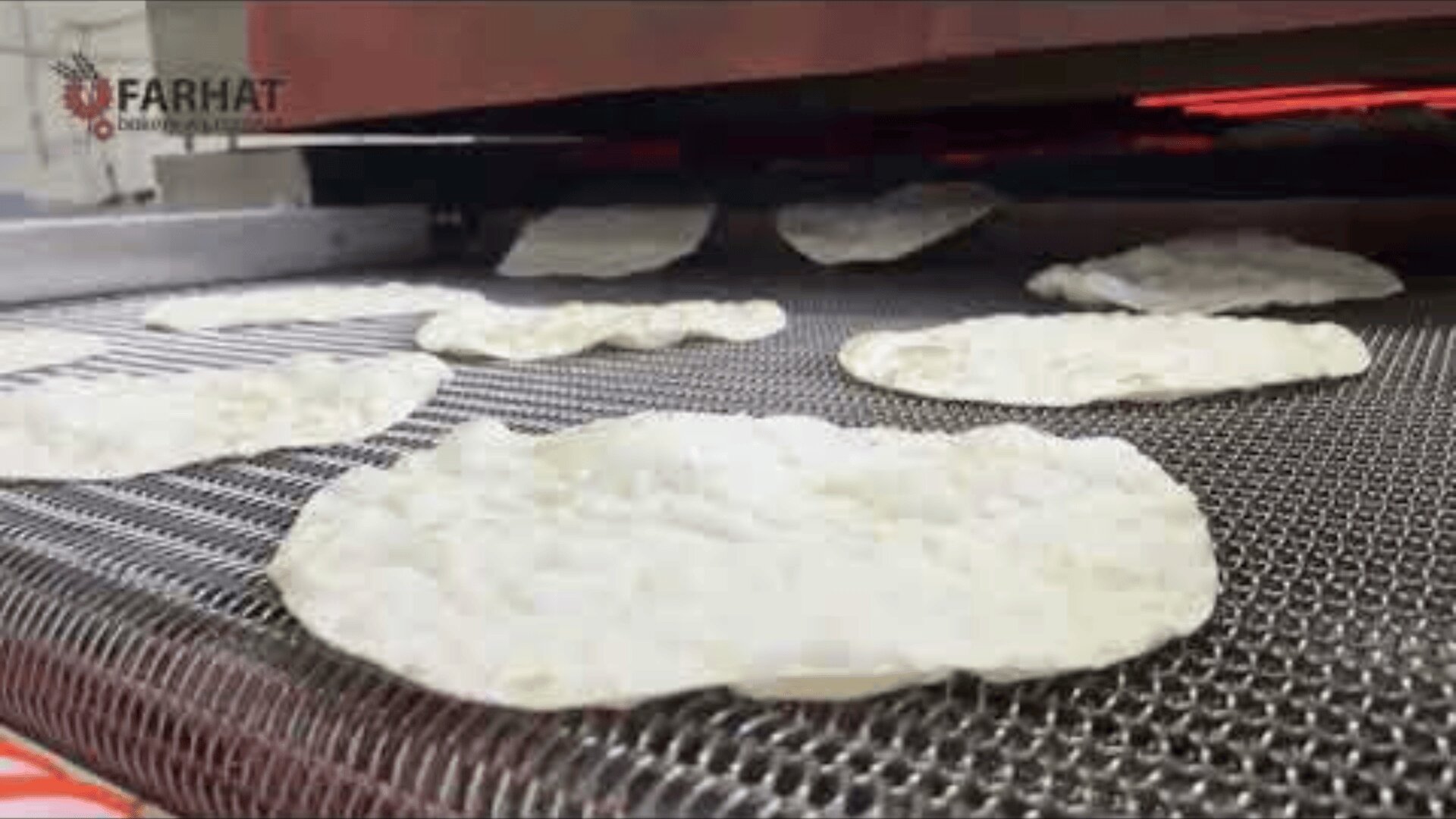 Flatbreads baking on a metal conveyor belt inside an industrial oven, with the Farhat brand logo visible in the upper left corner.
