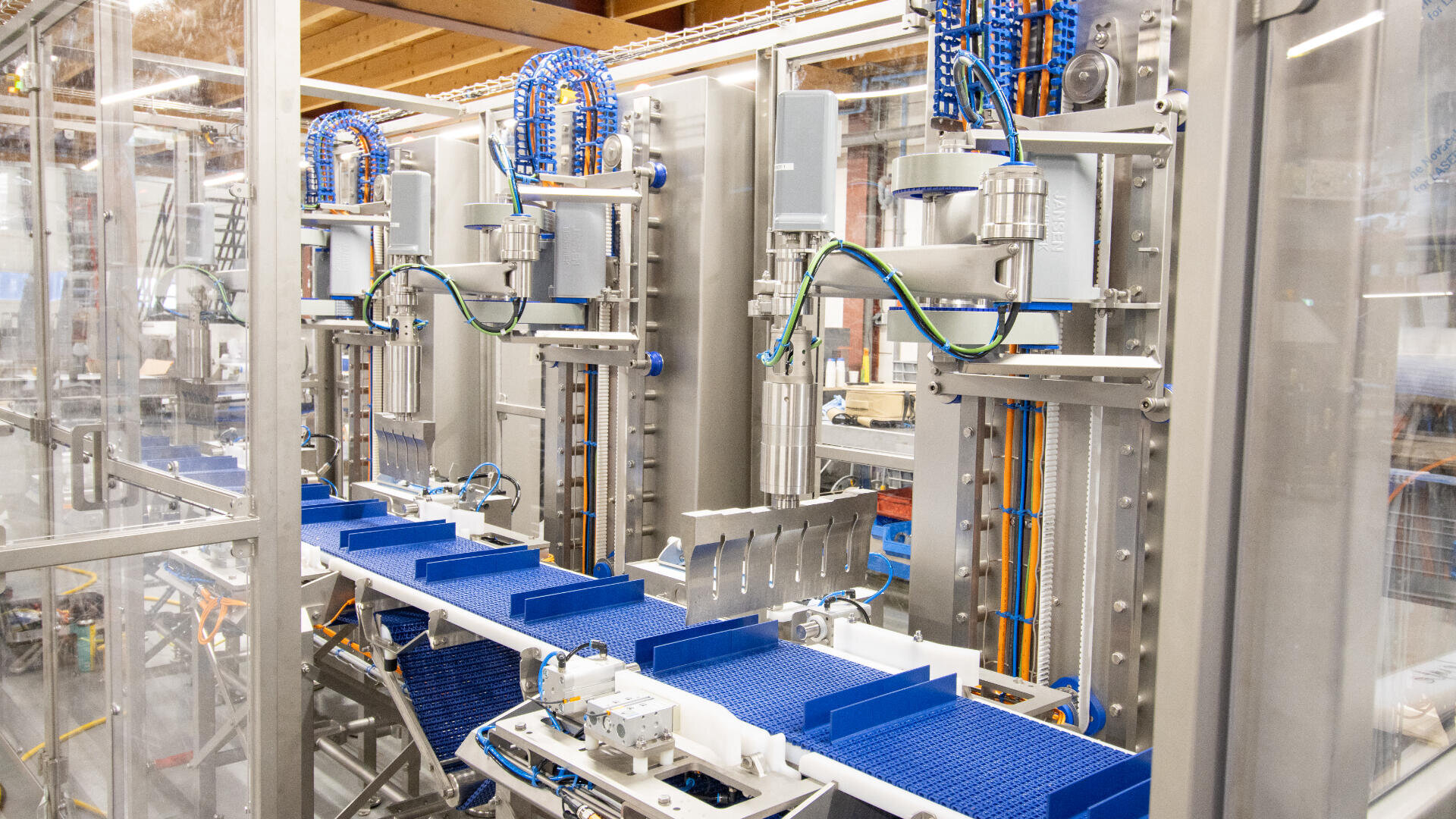 A modern automated production line with blue conveyor belts and advanced machinery inside a clean industrial facility, featuring exposed wiring and metal components.