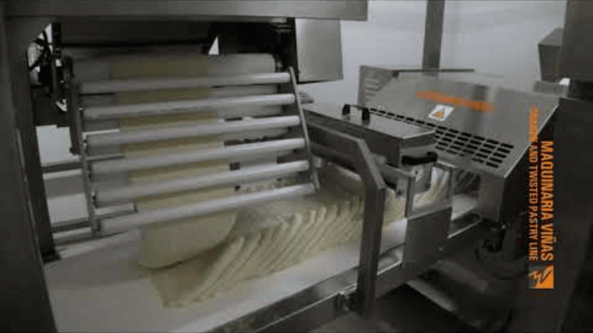 A dough sheeter that rolls out the dough into even layers and presses it flat. The machine has several rollers and is labeled MAQUINARIA VIÑAS INDUSTRIAL PASTELERA on the side.