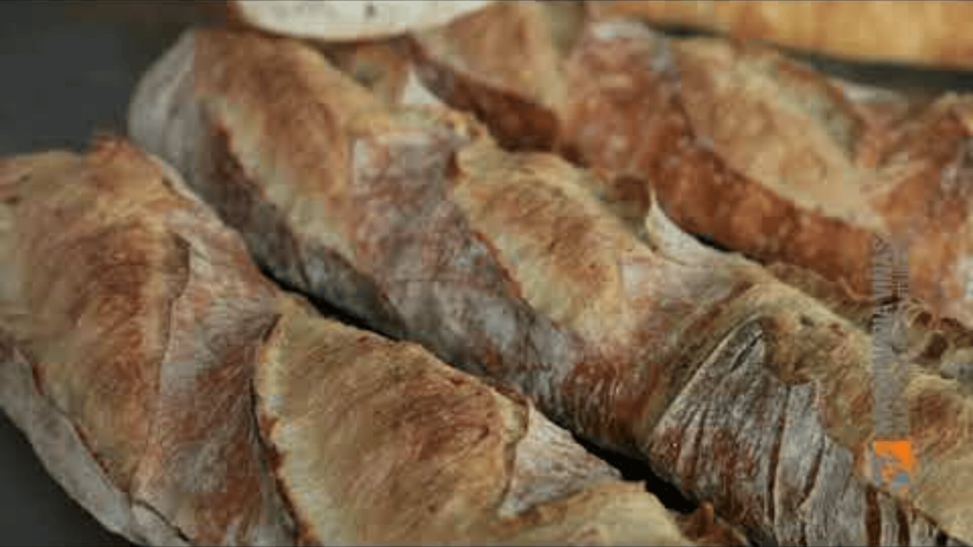 Three crispy, golden-brown baguettes with a crunchy, textured outside lie next to each other on a flat base. The bread looks freshly baked, rustic and homemade.