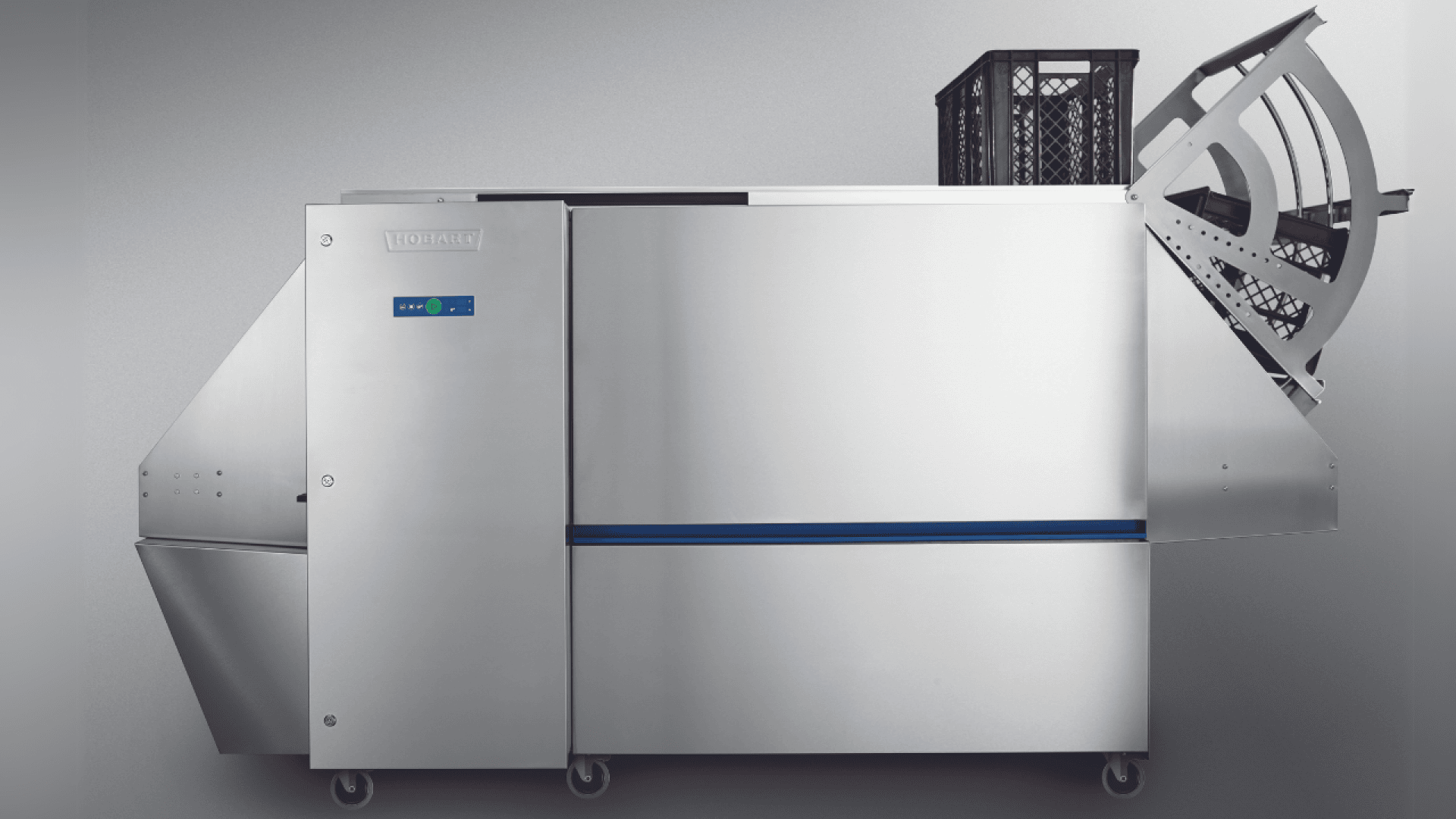 A large industrial dishwashing machine with a stainless steel exterior, a digital control panel, and an open rack loaded with dishes positioned on one end. The machine is set against a plain, light gray background.