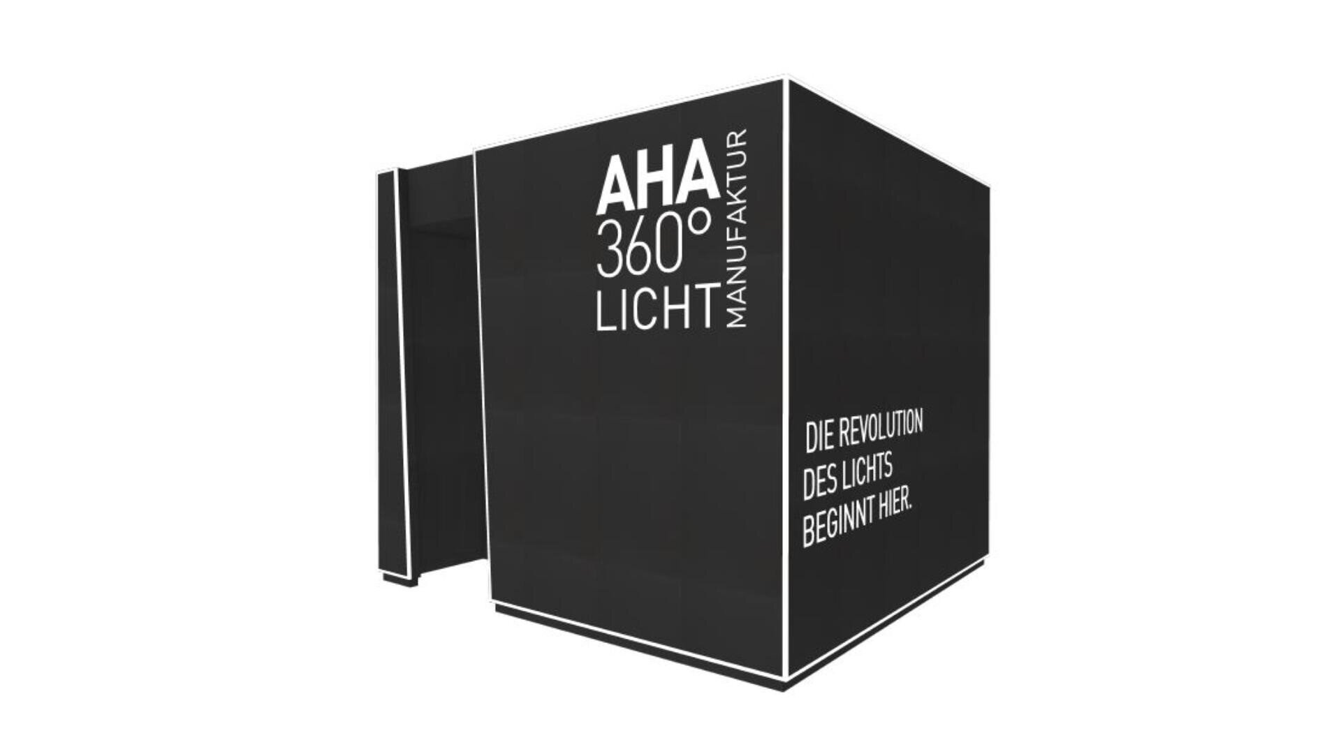 Ein großer, schwarzer, würfelförmiger Messestand mit den weißen Schriftzügen „AHA 360° LICHT MANUFAKTUR“ und „DIE REVOLUTION DES LICHTS BEGINNT HIER“ an den Seiten, vor weißem Hintergrund.