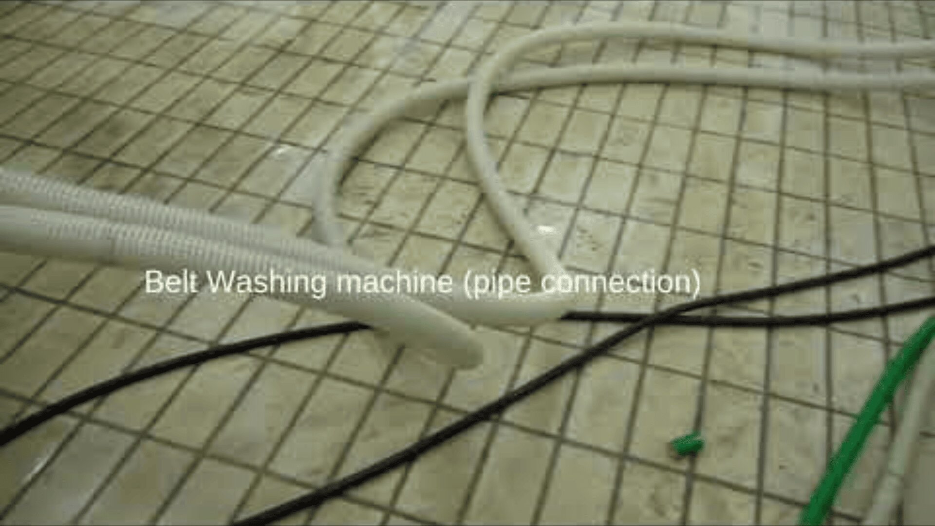 White and black pipes lay on a tiled floor with grid patterns. The text Belt Washing machine (pipe connection) is displayed over the image.