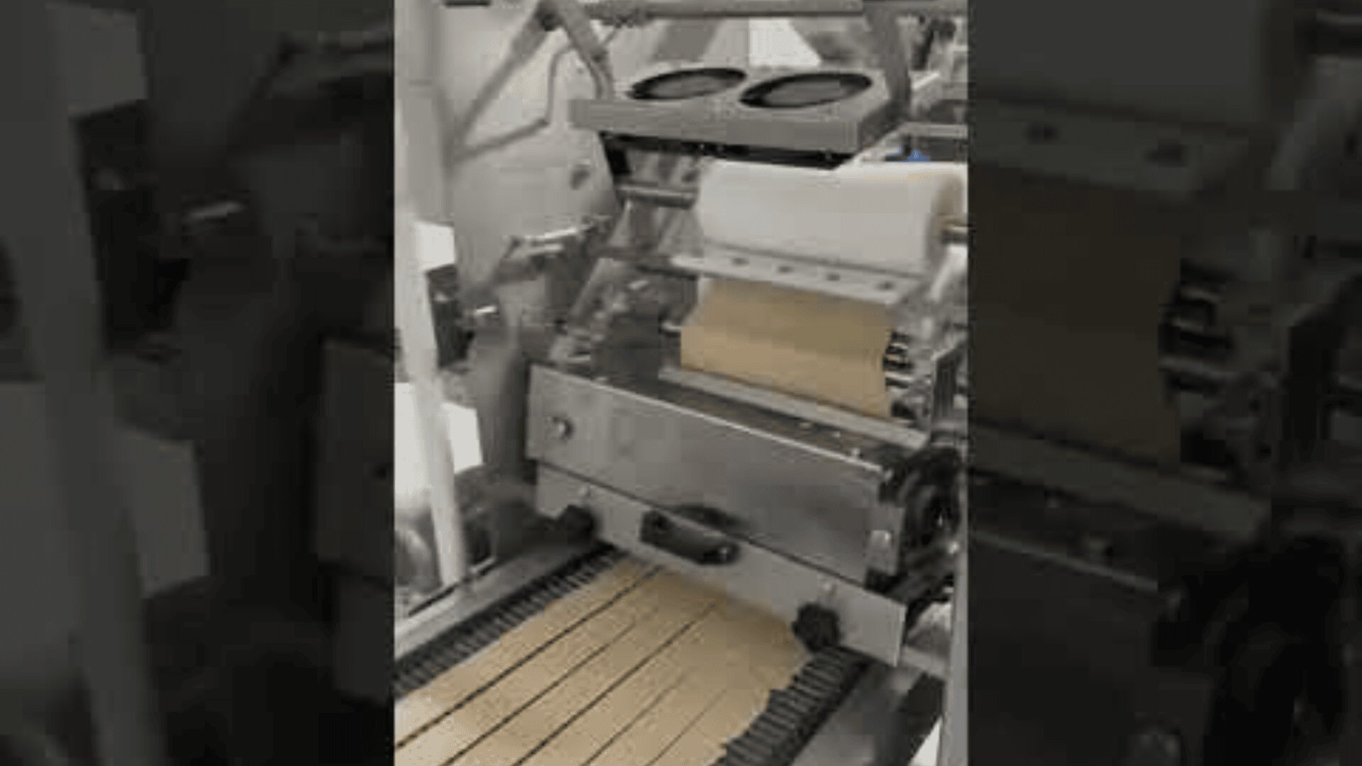 A food processing machine cuts rectangular crackers from a sheet of dough and places them onto a moving conveyor belt in a factory setting.