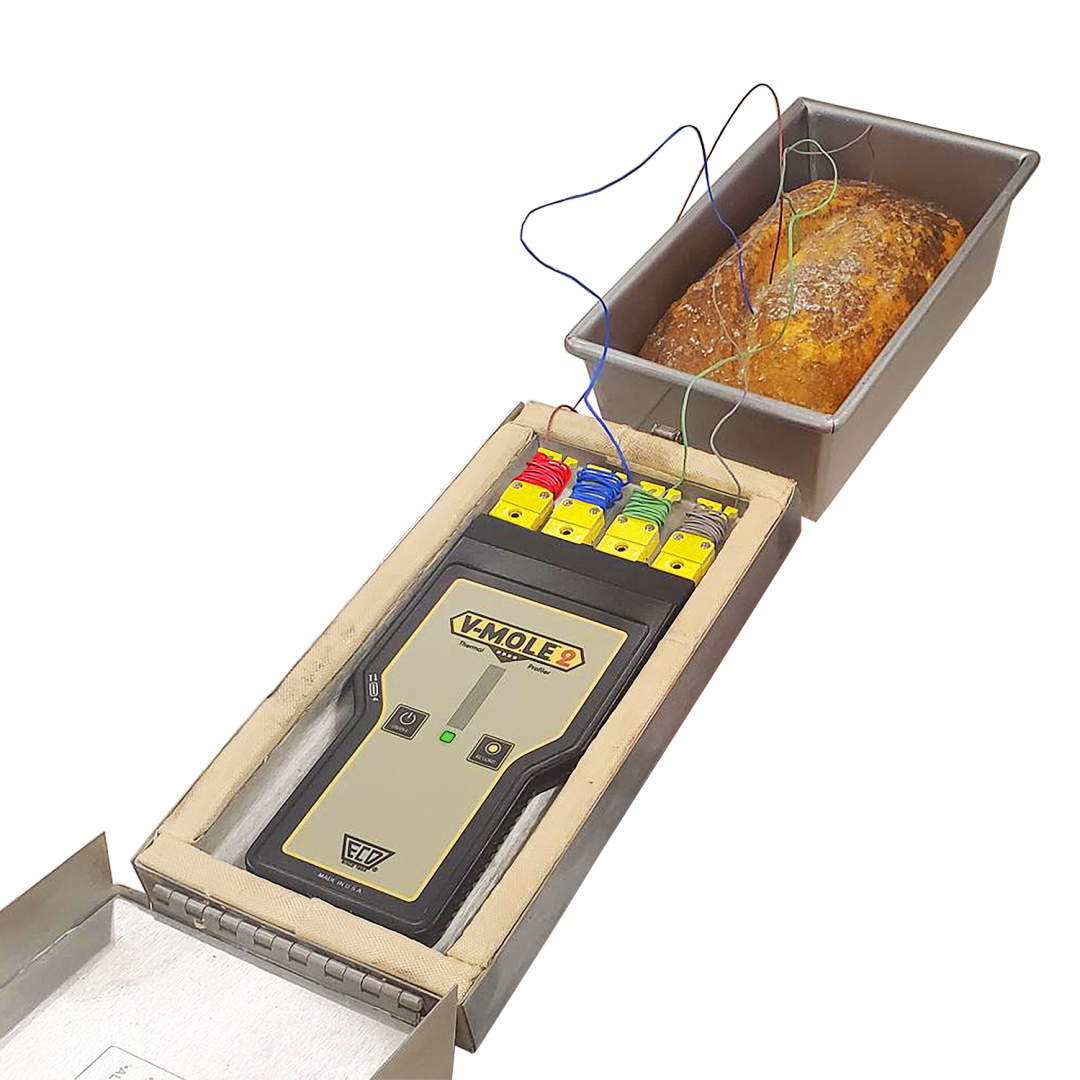 A loaf of bread in a metal pan with several wires inserted into it, connected to an electronic device labeled VMOLF2 with colored terminals on top.