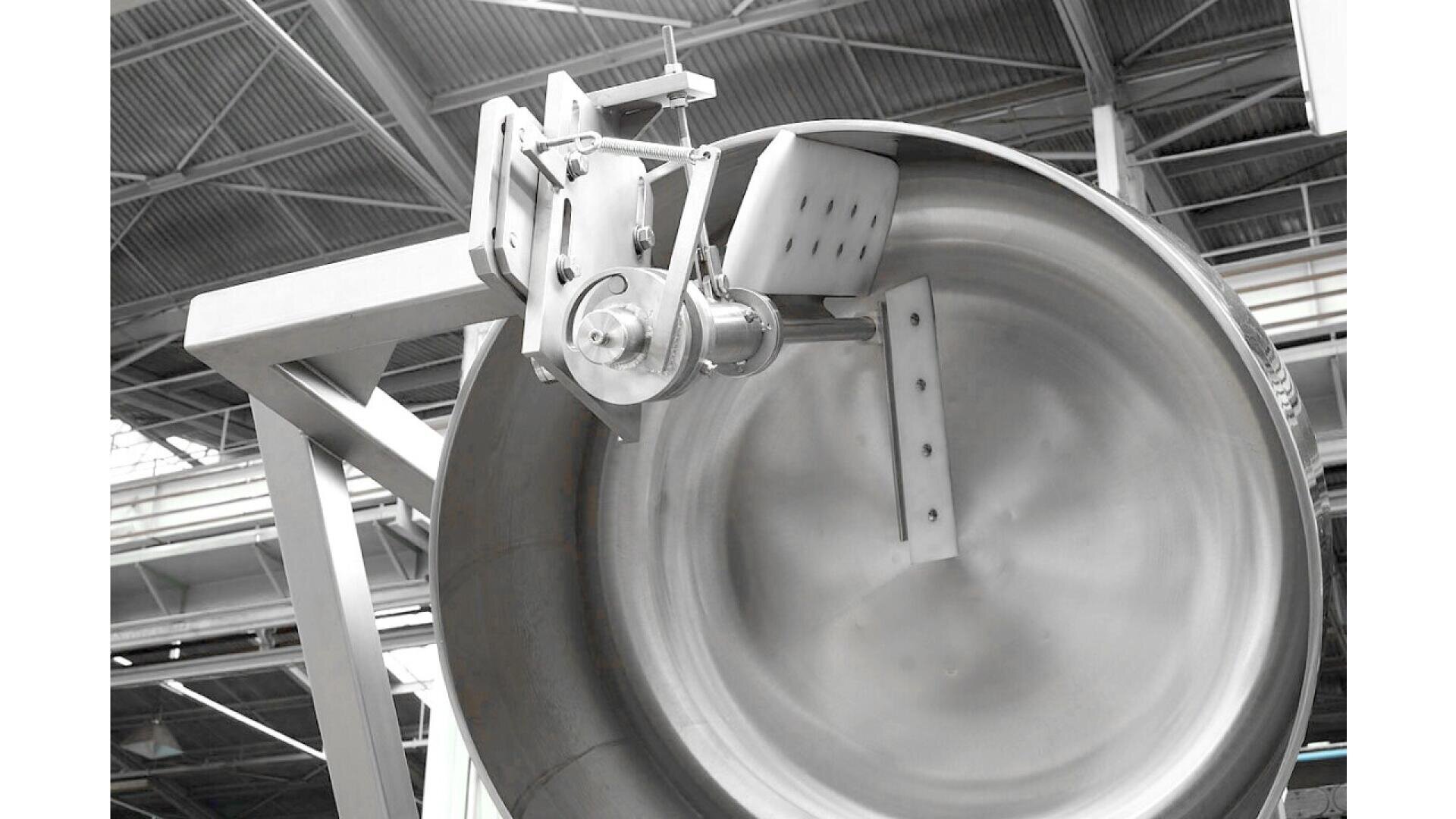 Eine große industrielle Mischmaschine mit Metallschaufeln, die in einer runden Trommel aus rostfreiem Stahl montiert ist, wird in einer Fabrik mit hoher Decke und freiliegenden Balken installiert.
