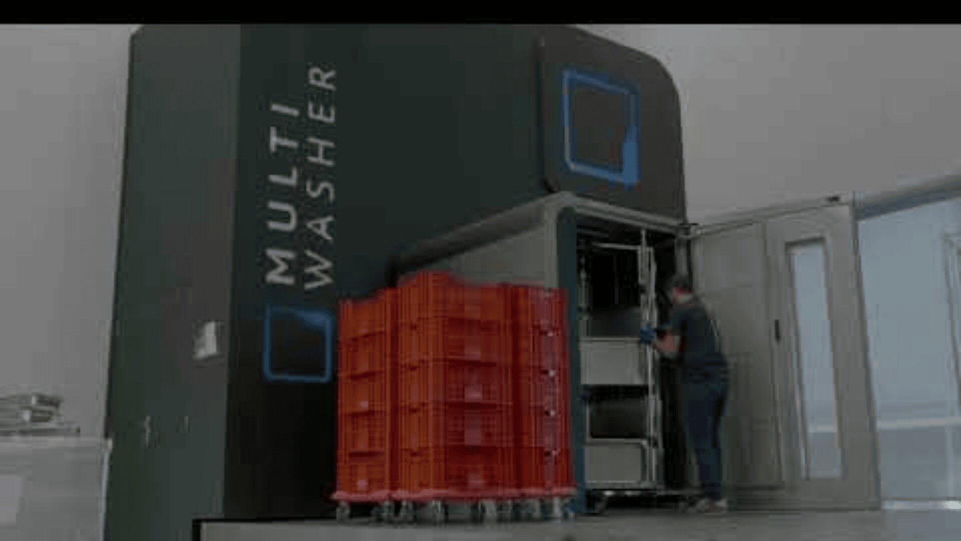 A person loads red plastic crates into a large industrial machine labeled Multi Washer inside a clean, modern facility.