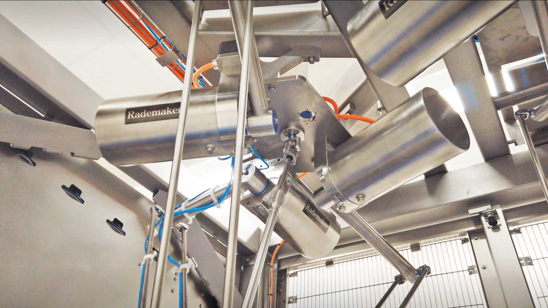 Close-up of stainless steel industrial machinery with tubes, wiring, and components, labeled “Rademaker,” inside a modern food processing or manufacturing facility.