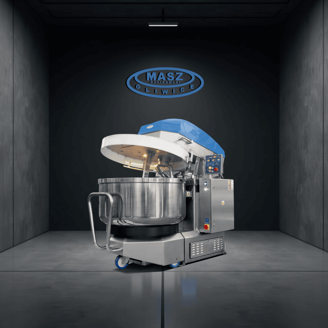 A large industrial dough mixer with a blue lid, stainless steel bowl, and digital controls stands in a modern, dark gray room with the MASZ GLIWICE logo on the wall behind it.
