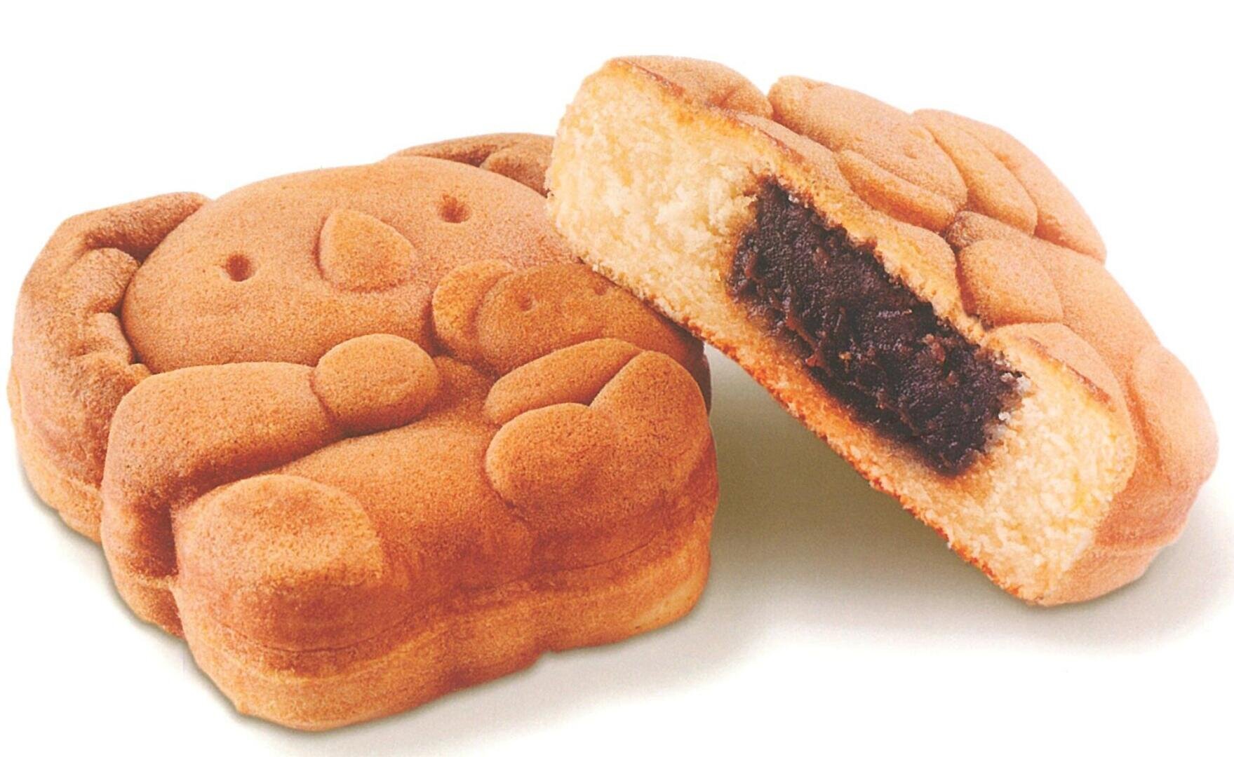 Two pastries shaped like koalas, one whole and one cut in half to reveal a dark sweet filling inside, set against a white background.