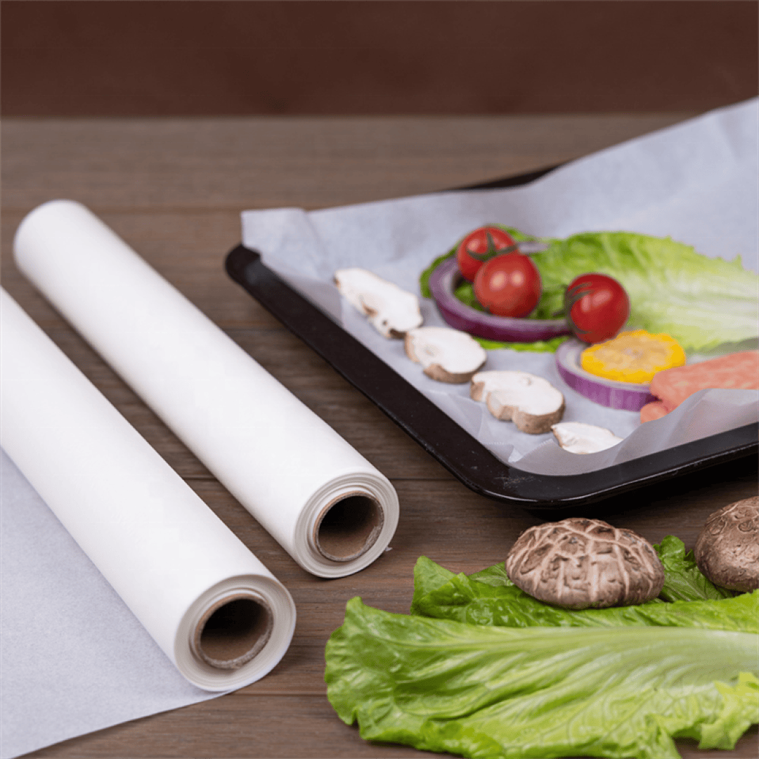 Two rolls of parchment paper sit on a wooden surface beside a tray lined with parchment paper and topped with fresh vegetables, including lettuce, tomato, mushroom, onion, and corn.