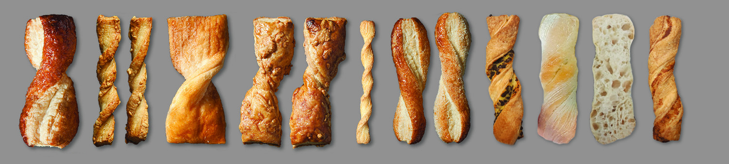 Ein Sortiment von vierzehn gedrehten Brotstangen und Fladenbrotstücken, die in einer Reihe auf grauem Hintergrund angeordnet sind und jeweils unterschiedliche Texturen, Drehungen und Brauntöne aufweisen.