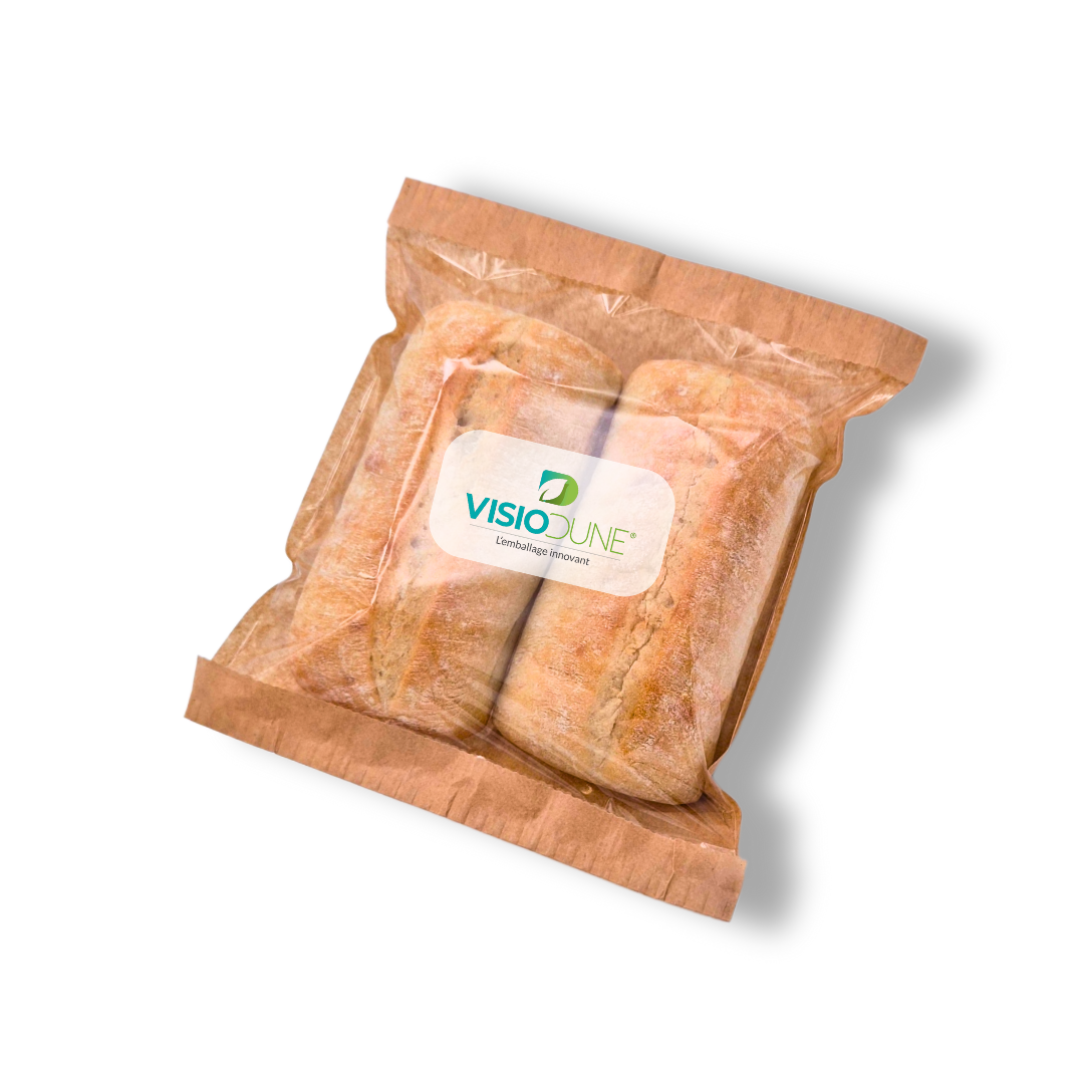 Two loaves of bread are sealed in a brown, eco-friendly paper bag with a transparent window and a label that reads VISIODUNE Emballages Innovants. The bag is placed on a white background.